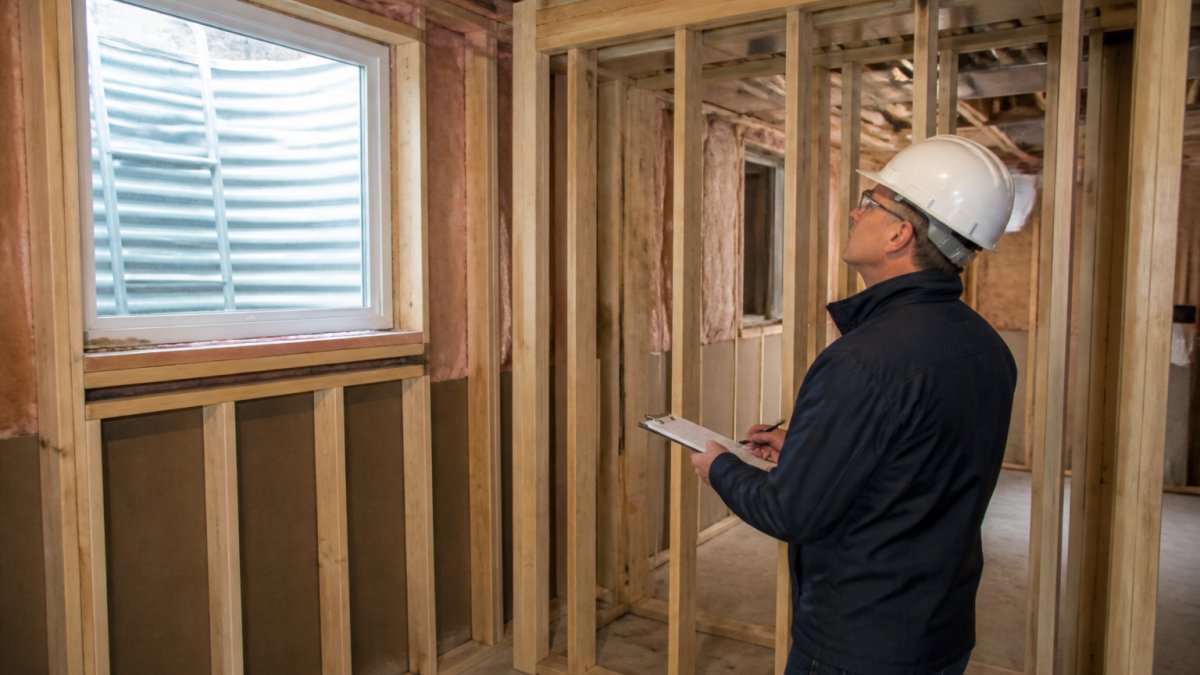 Professional inspector examining basement egress window installation and fire separation wall framing in a basement apartment under construction